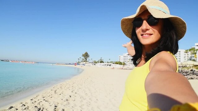 Young joyful caucasian woman in yellow shirt wear hat smiling at camera on the beach - Traveler girl enjoying freedom taking selfie - Well being, healthy lifestyle and happy people
