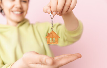 Close-up focus on keys with a house-shaped key chain in female hands, moving into a new apartment, creating the concept of a real estate bank mortgage loan transaction.