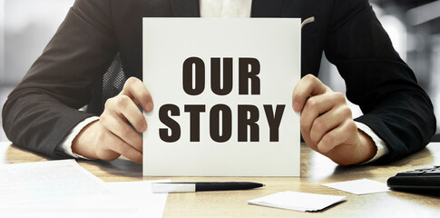 Businessman holding a white card with text OUR STORY on office background