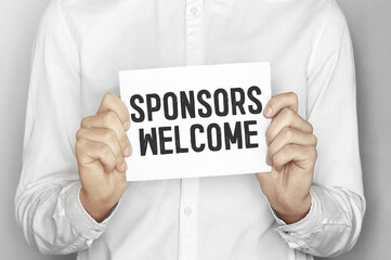 Man holding a paper card with text SPONSORS WELCOME