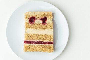 Flat lay of a cake slice on the white plate on the white background. Biscuit sponge cake cut with cream cheese and red berry mousse layers. confectionery menu template