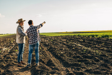 Two farmers on a field looking at their farmland