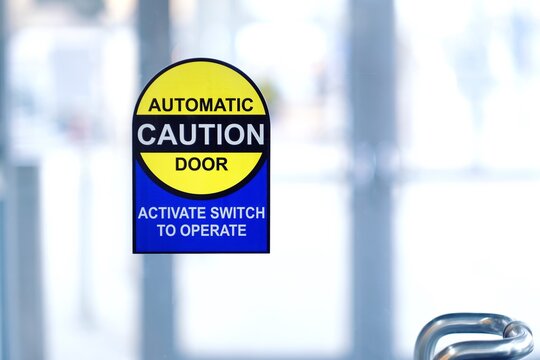 Yellow and blue caution sign on automatic door with activate switch to operate instruction.