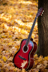 Detail of a guitar in the park on a background of fallen autumn leaves. Autumn music concept