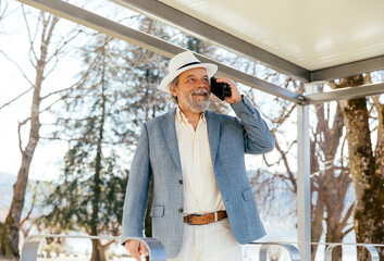 Portrait of a confident, handsome, mature man, pensioner, grandfather in the small town calling someone on the phone