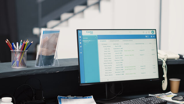 Medical appointments on computer at desk, empty reception area in diagnostic center. Waiting room registration counter with list of patients, healthcare checkup visit examination.
