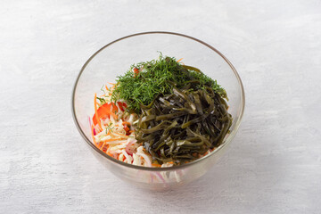 Glass bowl with shredded cabbage, grated carrots, chopped sweet peppers, red onion, seaweed and dill on light gray background. Step of preparing healthy vegan salad