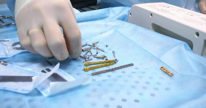 The hand of a veterinary surgeon takes a screw from the table with instruments to install a plate on a broken bone. In the veterinary clinic in the operating room there is an instrument on the table.