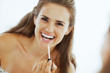 Happy young woman applying lip gloss in bathroom