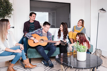 Group of young friends sitting in the living room drinking beers and playing guitar. Concept: lifestyle, fun, friendship