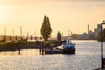 Naklejka premium River harbour at sunset in summer. A lighthouse, industrial plants and wind turbines are visible in background.