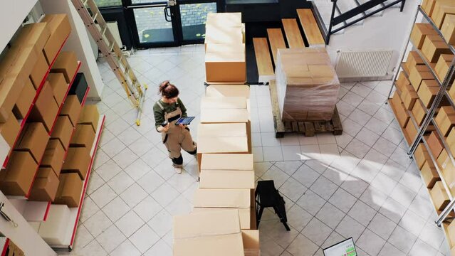 Delivery team checking depot products, reviewing supplies and cargo in boxes with computers. Man and woman verifying merchandise production for retail store distribution. Drone shot. Top view.