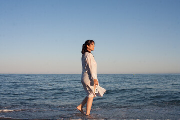 mujer con vestido blanco en la playa al atardecer en verano mirando con tranquilidad