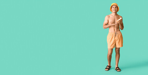 Happy young man with sunscreen cream on turquoise background with space for text