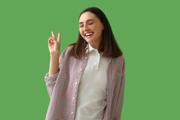 Happy young woman showing victory gesture on green background