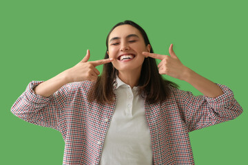 Young woman pointing at her teeth on green background