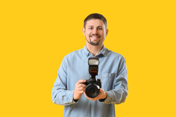 Male photographer with professional camera on yellow background
