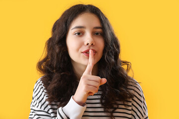 Fototapeta premium Young woman with finger on lips signaling silence, secrecy, and confidentiality on yellow background
