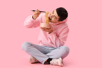 Young man eating Chinese noodles on pink background