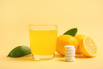 Glass of vitamin C effervescent tablet dissolved in water and lemons on beige background