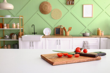 Board with cut tomatoes and knife on white table in kitchen