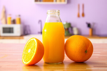Bottle of fresh orange juice and fruits on wooden table in kitchen