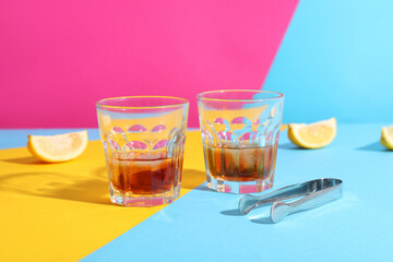 Fototapeta na wymiar Glasses of rum with ice cubes, tongs and lemon slices on colorful background