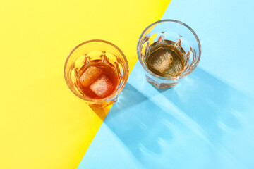Glasses of rum with ice cubes on blue and yellow background
