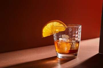 Glass of rum with ice cubes and orange slice on brown background