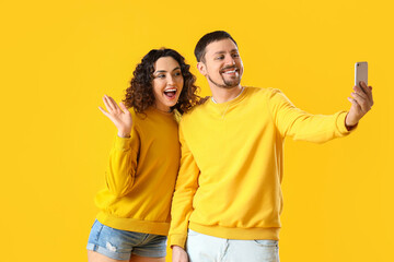 Young couple with mobile phone taking selfie on yellow background