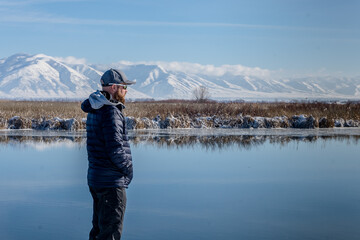 man standing outdoors next to river in winter mountains