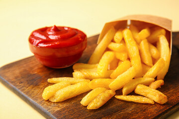 Wooden board with paper box of tasty french fries and ketchup on color background, closeup