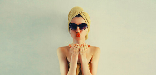 Fototapeta premium Portrait of stylish beautiful woman drying her wet hair with wrapped towel on her head having fun in trendy sunglasses on gray background