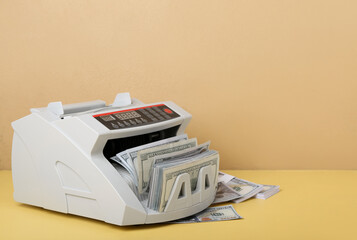 Modern cash counting machine with dollar banknotes on color background