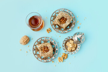 Plates with tasty baklava and glass of Turkish tea on blue background