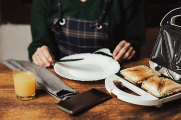 Fototapeta na wymiar Sandwich and juice. Snack and breakfast preparation. Sandwich maker and unrecognizable woman on wooden background.