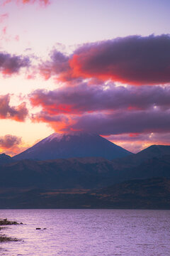 volcan tapado con nubes en atardecer al pie de un lago