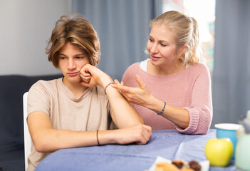 Mother and unhappy teenage son sitting after quarrel at home, mother consoles son