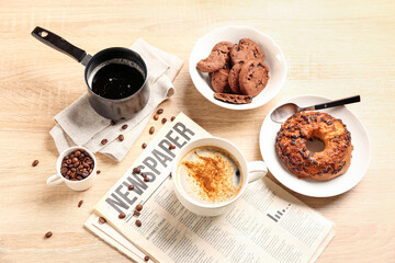 Cup of coffee with newspaper, pastry, beans and cezve on light wooden background