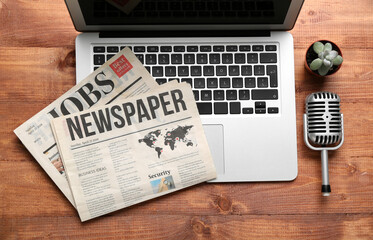 Laptop with newspapers and microphone on wooden background