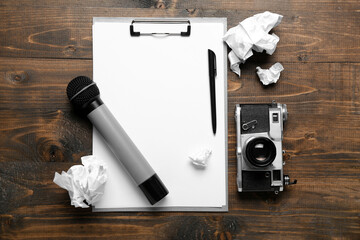 Clipboard with microphone, crumpled paper and photo camera on dark wooden background