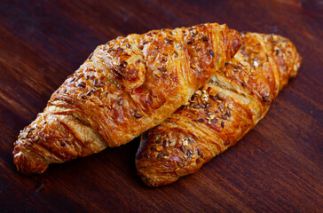 Fresh wholegrain croissants decorated with seeds of brown and gold flax on wooden surface