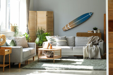Interior of light living room with surfboard, houseplants and sofas