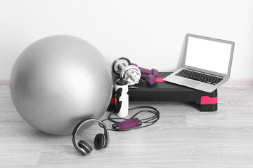 Laptop with sports equipment and headphones near white wall in gym