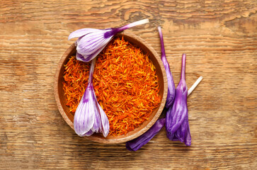 Bowl of dried saffron threads with crocus flowers on wooden table