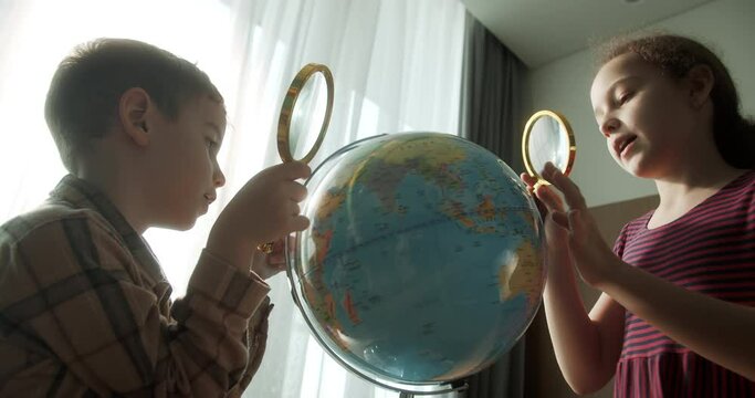 Children is studying while sitting at home in rays sunset in room.Kids in morning light sunset. Cute Children with Globe and magnifying glass, technology for schoolboy, child looks at globe. 4K