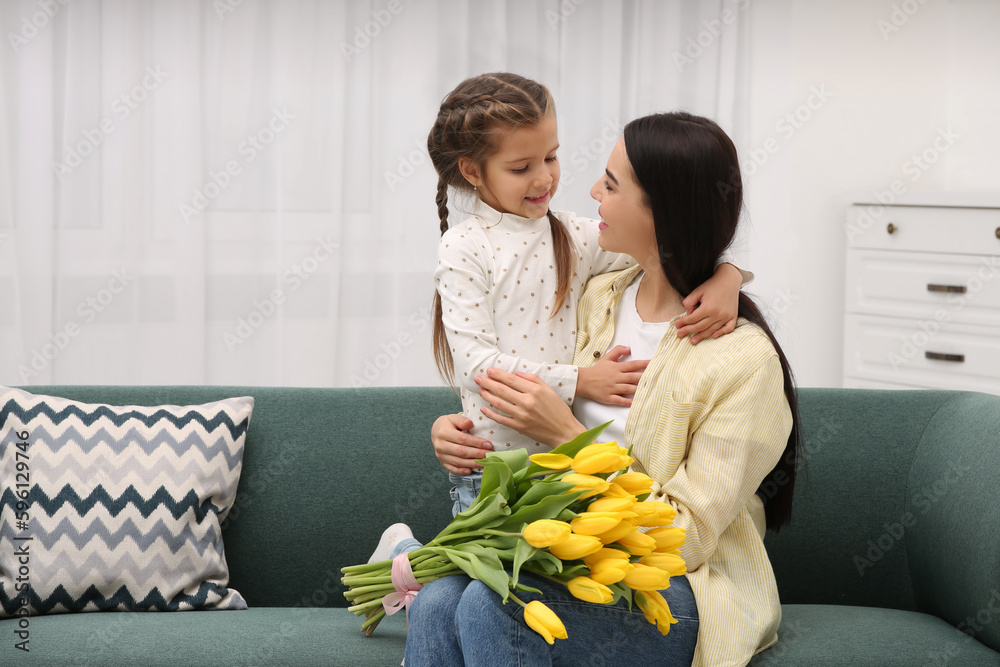 Poster Happy woman with her daughter and bouquet of yellow tulips on sofa at home, space for text. Mother's day celebration