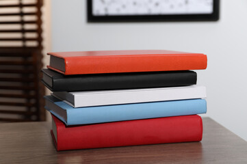 Stack of different hardcover books on wooden table indoors