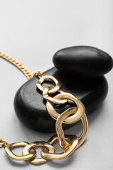 Black stones with golden necklace on light background, closeup