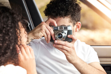 The best memories are the ones made on road trips. a young man taking a picture of his girlfriend while sitting in a car together.